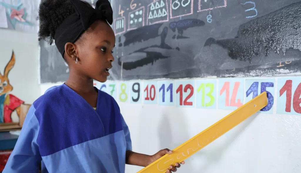 Ndeye, 4 ans, en grande section, identifie les chiffres sur un tableau à l’aide d’une règle